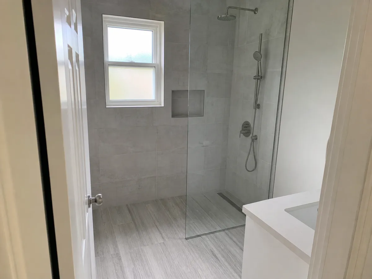 A finished curbless walk-in shower with large grey tile, a glass panel, a recessed niche and a brushed nickel rain head